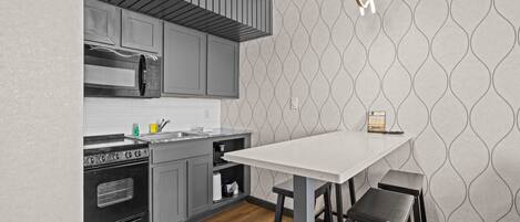 A kitchen with grey cabinets, a white countertop, a wooden ceiling, and a patterned wall.