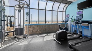 Een sportschool met trainingsapparatuur, een loopband en uitzicht op het strand.