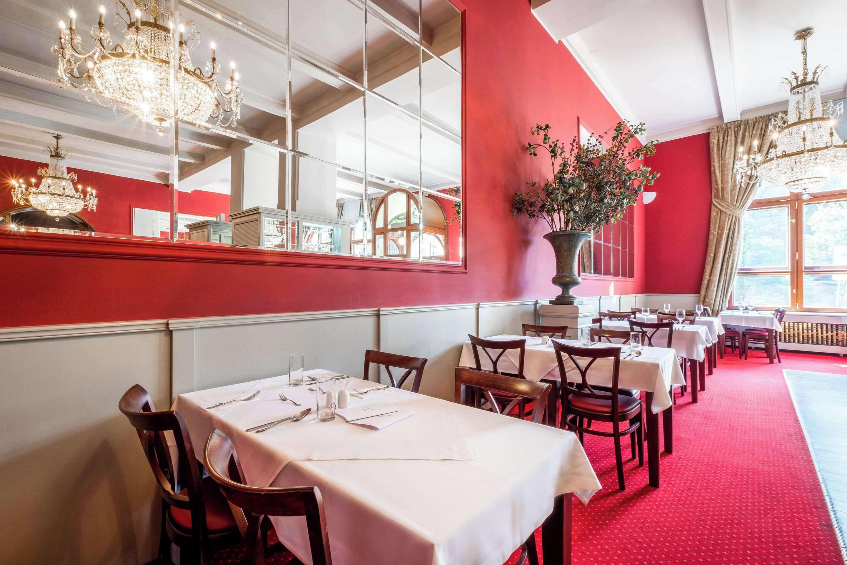 A restaurant with red walls, white tables, and chandeliers.