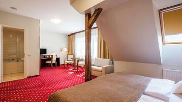 A hotel room with a red carpet, a bed, a desk with a chair, a sofa, and a window with curtains.