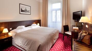 A hotel room with a large bed, two bedside tables with lamps, a TV, a desk with a chair, and a red carpet.
