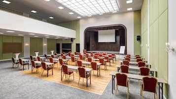 Un salón de conferencias con mesas, sillas, un escenario y una pantalla grande.