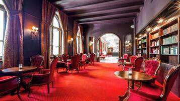 Un vestíbulo de hotel con alfombra roja, sillas clásicas rojas, mesas de madera y estanterías.