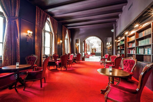 A hotel lobby with red carpet, classic red chairs, wooden tables, and bookshelves. - Clarion Grandhotel Zlaty Lev (Liberec)