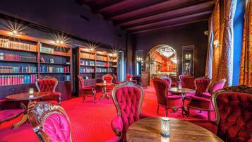 Eine Bibliothek mit Bücherregalen, roten Polstersesseln und einer Kristallleuchtre.