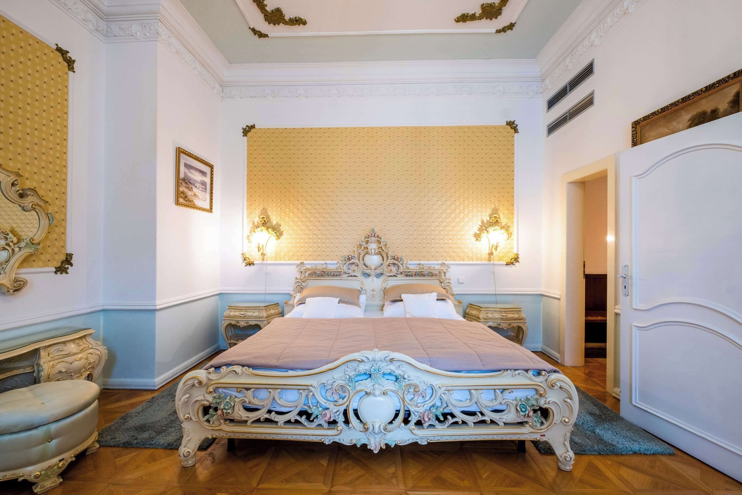 Una cama grande y ornamentada con un cabecero alto, dos lámparas de noche y un espejo grande sobre la cama.