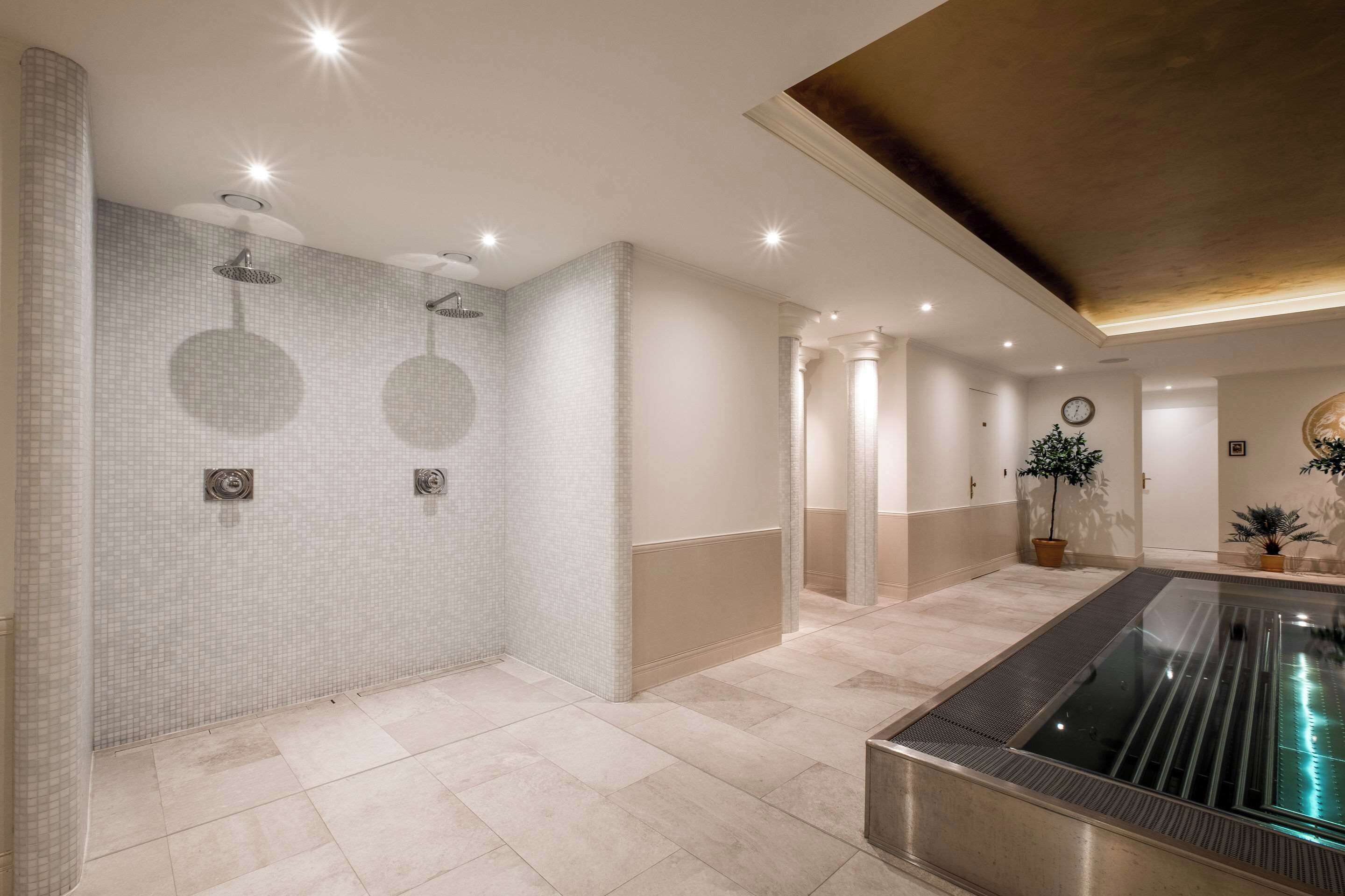 Un moderno espacio de spa con una amplia piscina climatizada, paredes con azulejos e iluminación empotrada.