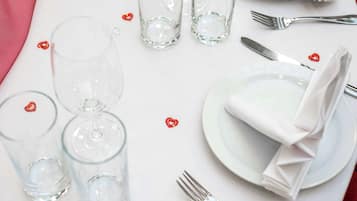 Una mesa dispuesta con vasos traslúcidos, platos y servilletas dobladas, con pequeñas decoraciones en forma de corazón rojo.