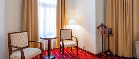 A hotel room with two chairs, a small round table, a lamp, and a coat stand.