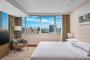 A hotel room with a large bed, a chair, a TV, and a view of the city skyline through large windows. - Four Points by Sheraton Shanghai, Daning (Shanghai)
