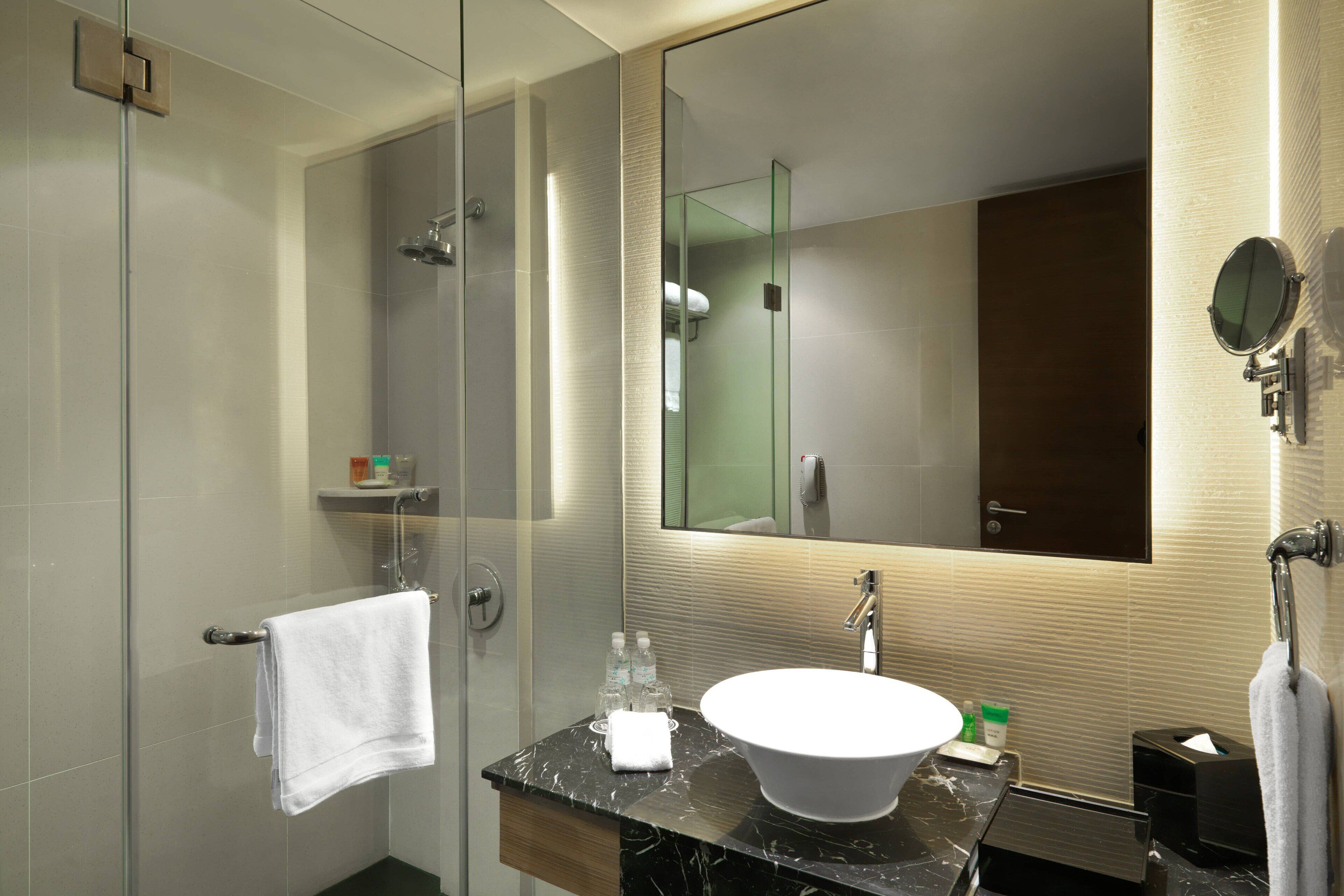 A modern bathroom with a glass shower enclosure, a marble sink, and a large mirror.