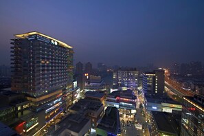 Un hotel de gran altura con varios pisos y balcones, rodeado de otros edificios y calles concurridas de noche.