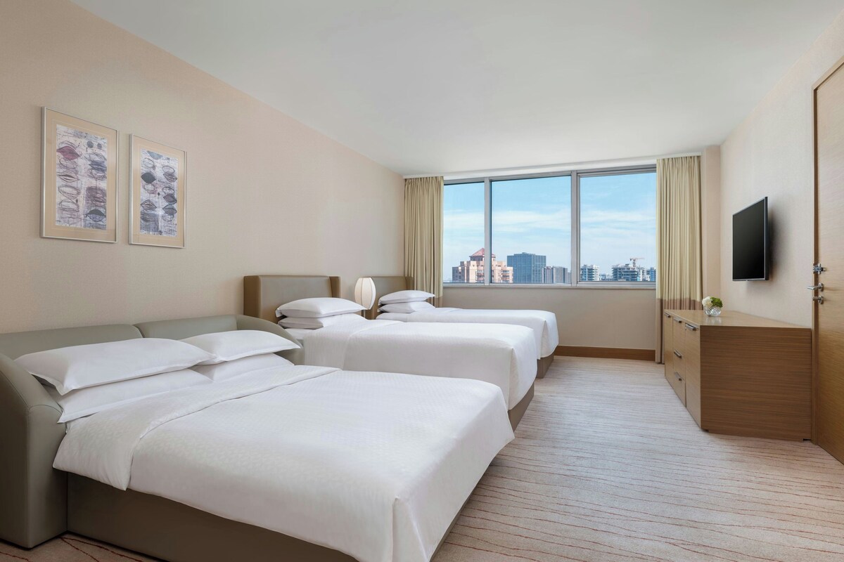 A hotel room with two beds, a TV, and a city view.