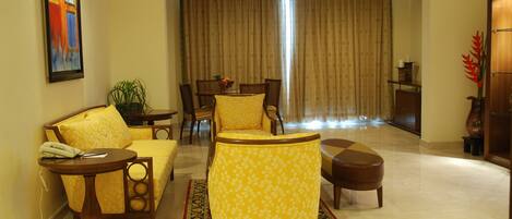 A living room with yellow patterned furniture, a dining area with a table and chairs, and a large window with curtains.