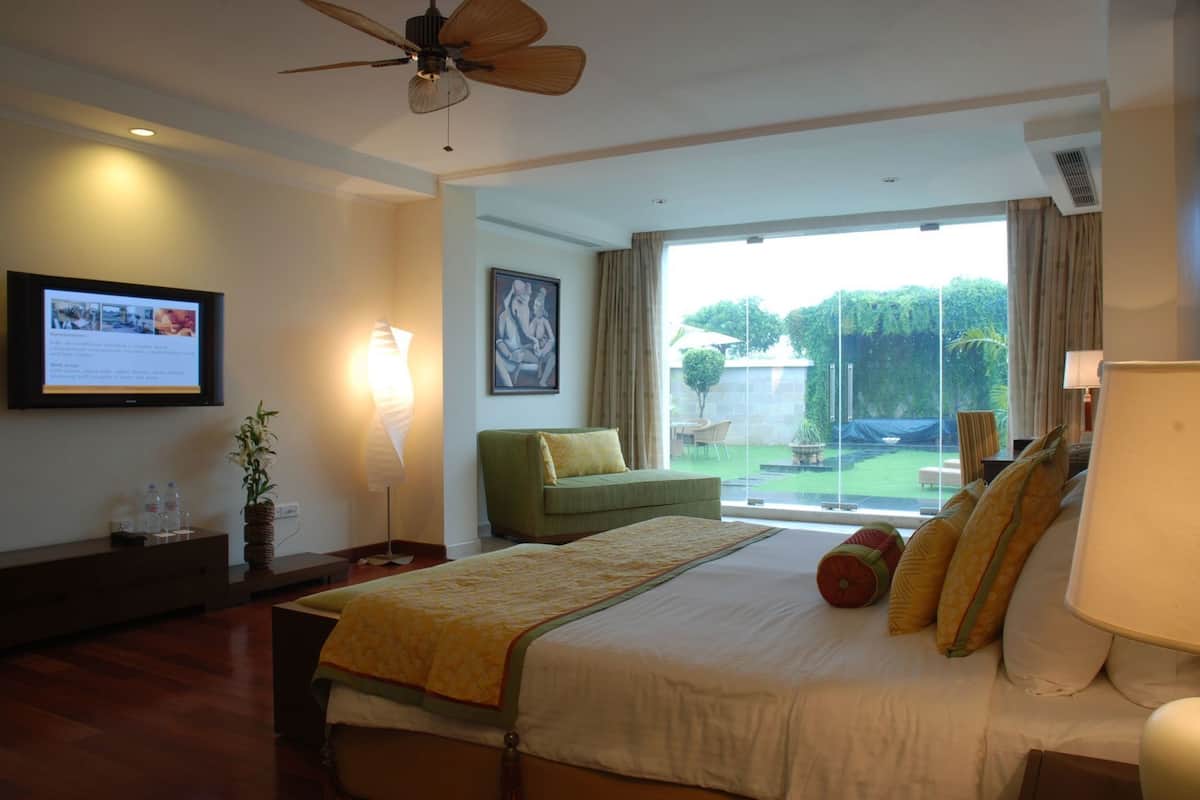 A hotel room with a bed, a television, a ceiling fan, a green sofa, and a view of a garden.
