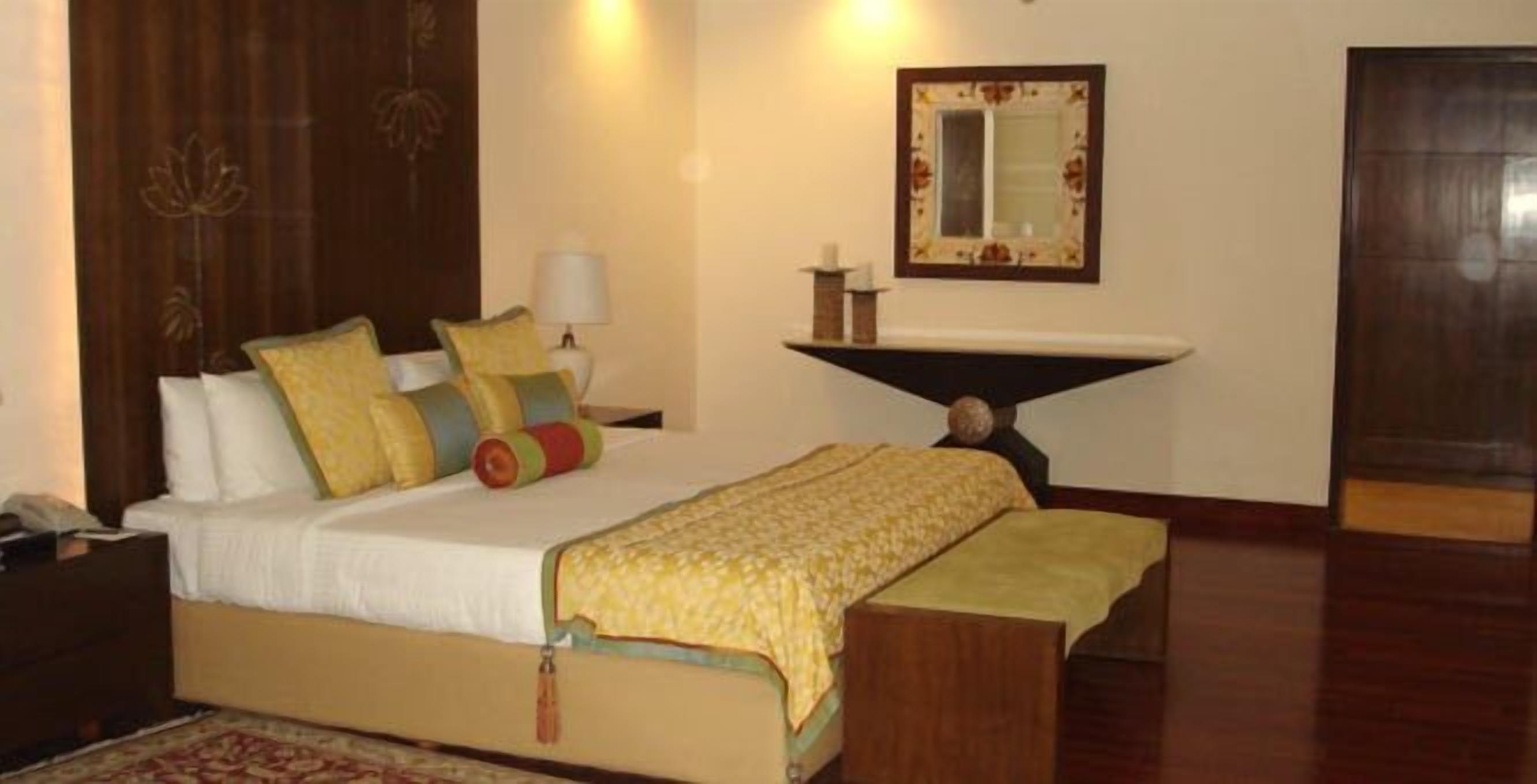 Una habitación de hotel con cama, mesita de noche, lámpara, espejo y una pequeña mesa con una vela.