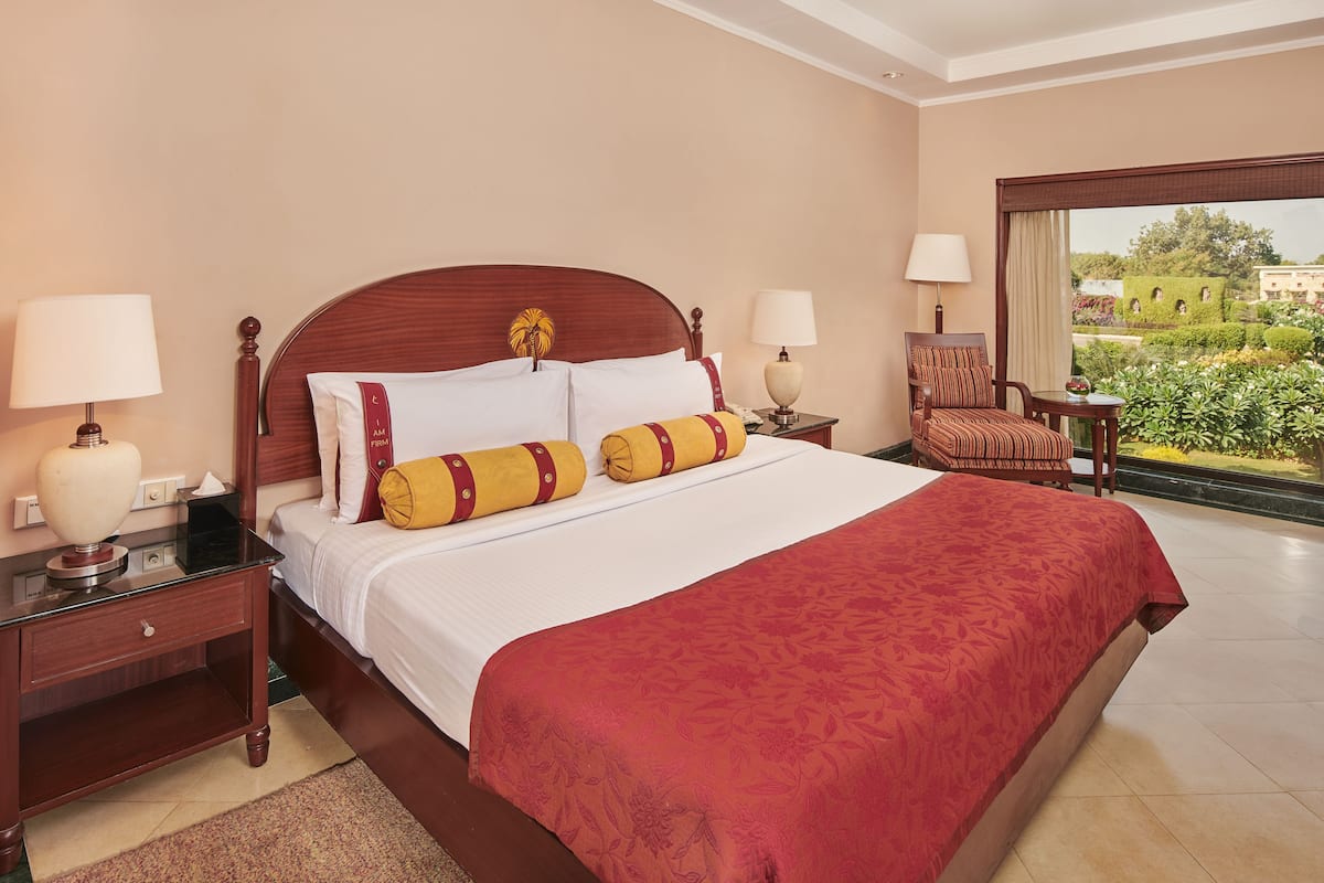 A hotel room with a large bed, two bedside tables with lamps, a chair, and a view of a garden through a large window.
