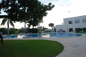 Una piscina con césped, palmeras y un edificio moderno al fondo.