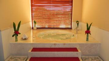 Un área de spa con una bañera, escalones con alfombra roja y arreglos florales.
