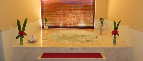 Un área de spa con una bañera, escalones con alfombra roja y arreglos florales.