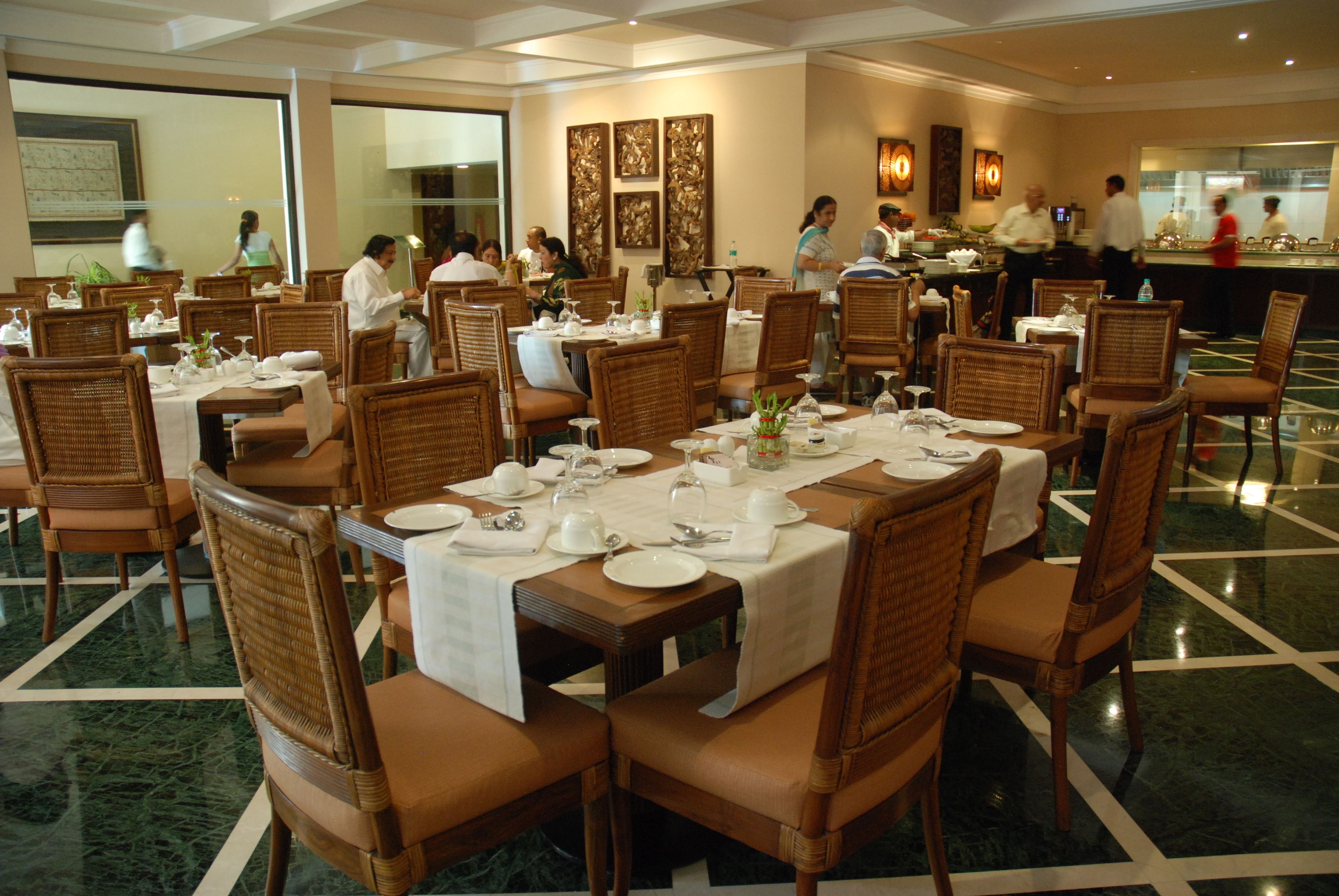 A dining area with tables set for multiple guests, featuring wicker chairs and a marble floor.