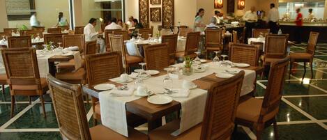 Comedor con mesas dispuestas para varios comensales, con sillas de mimbre y piso de mármol.