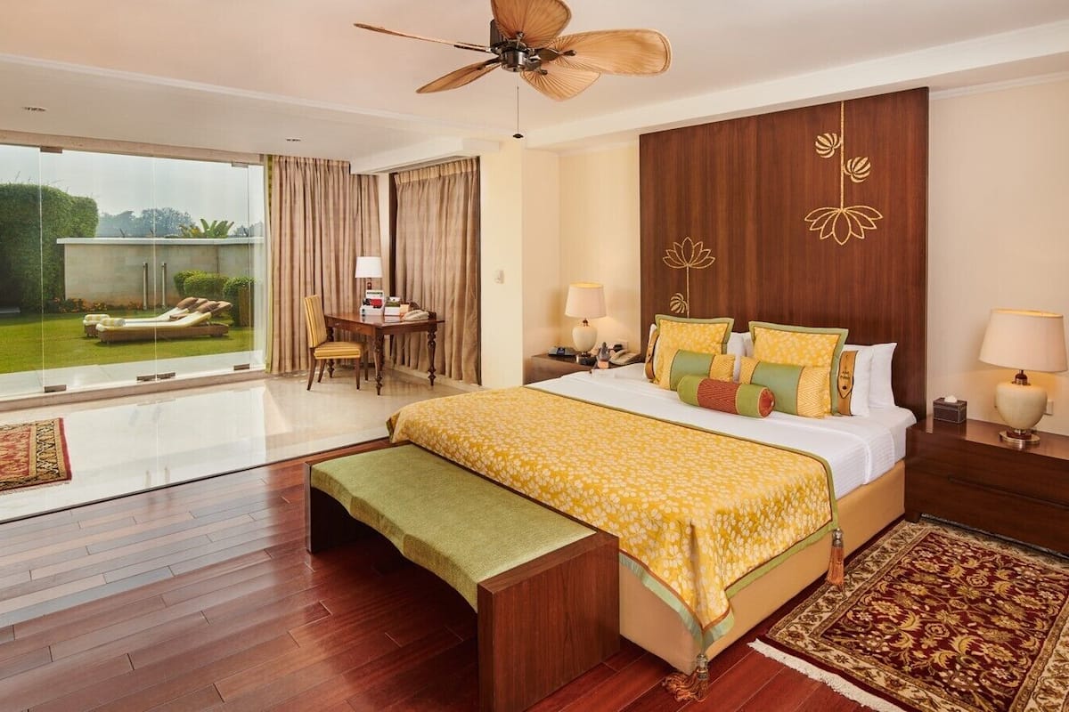 A hotel room with a large bed, a desk, a chair, and a view of the garden.
