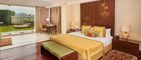 A hotel room with a large bed, a desk, a chair, and a view of the garden.