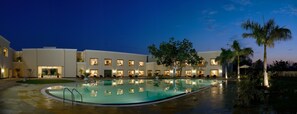 Un hotel moderno con una piscina grande, varias habitaciones y zonas de estar al aire libre.