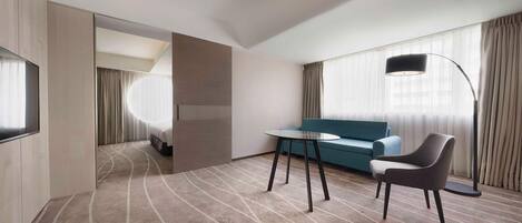 A modern hotel room with a curved carpet, a sofa, a chair, a table, and a TV.