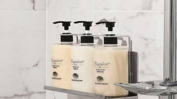 Un baño con tres botellas de champú y jabón líquido sobre una repisa.