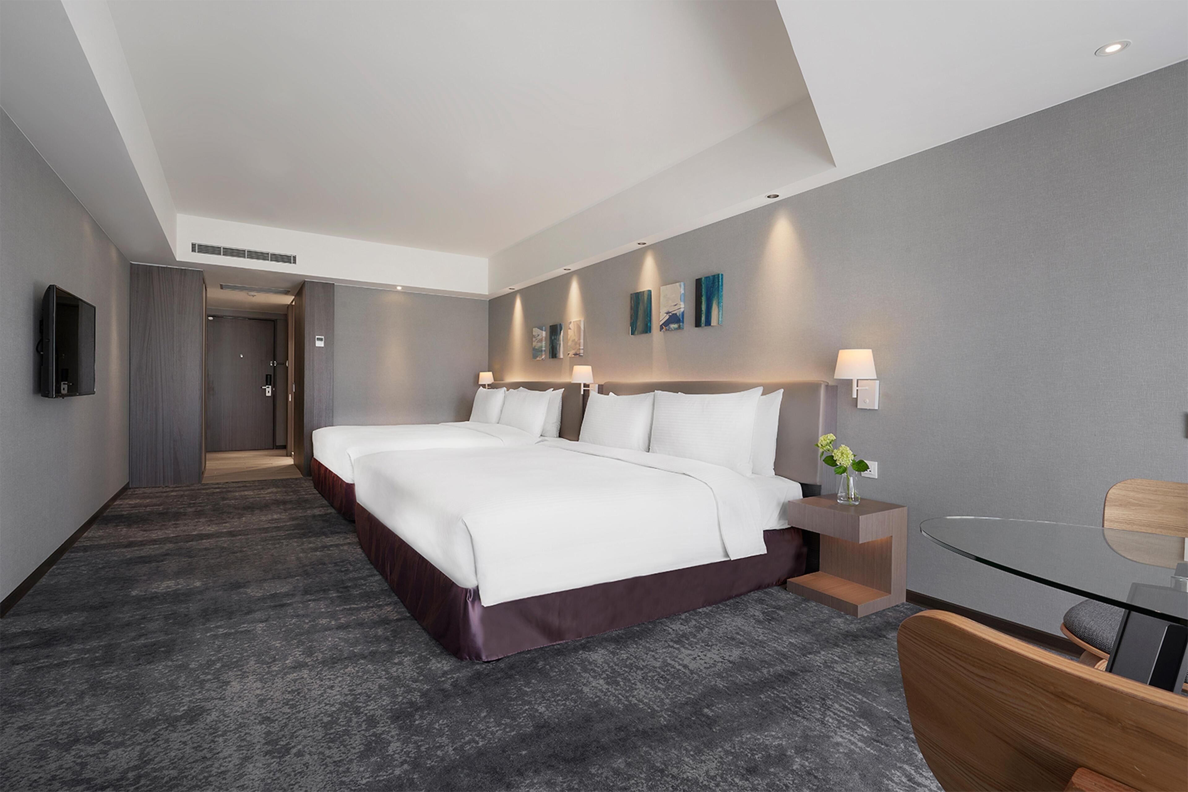 A modern hotel room with a large bed, bedside tables, a desk, and a TV.