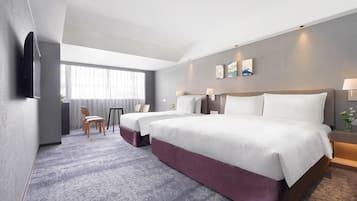 Habitación de hotel con dos camas, un escritorio, una silla y un ventanal amplio.