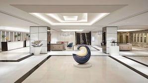 Een moderne lobby met een centrale sculptuur, een receptiebalie en een trap.