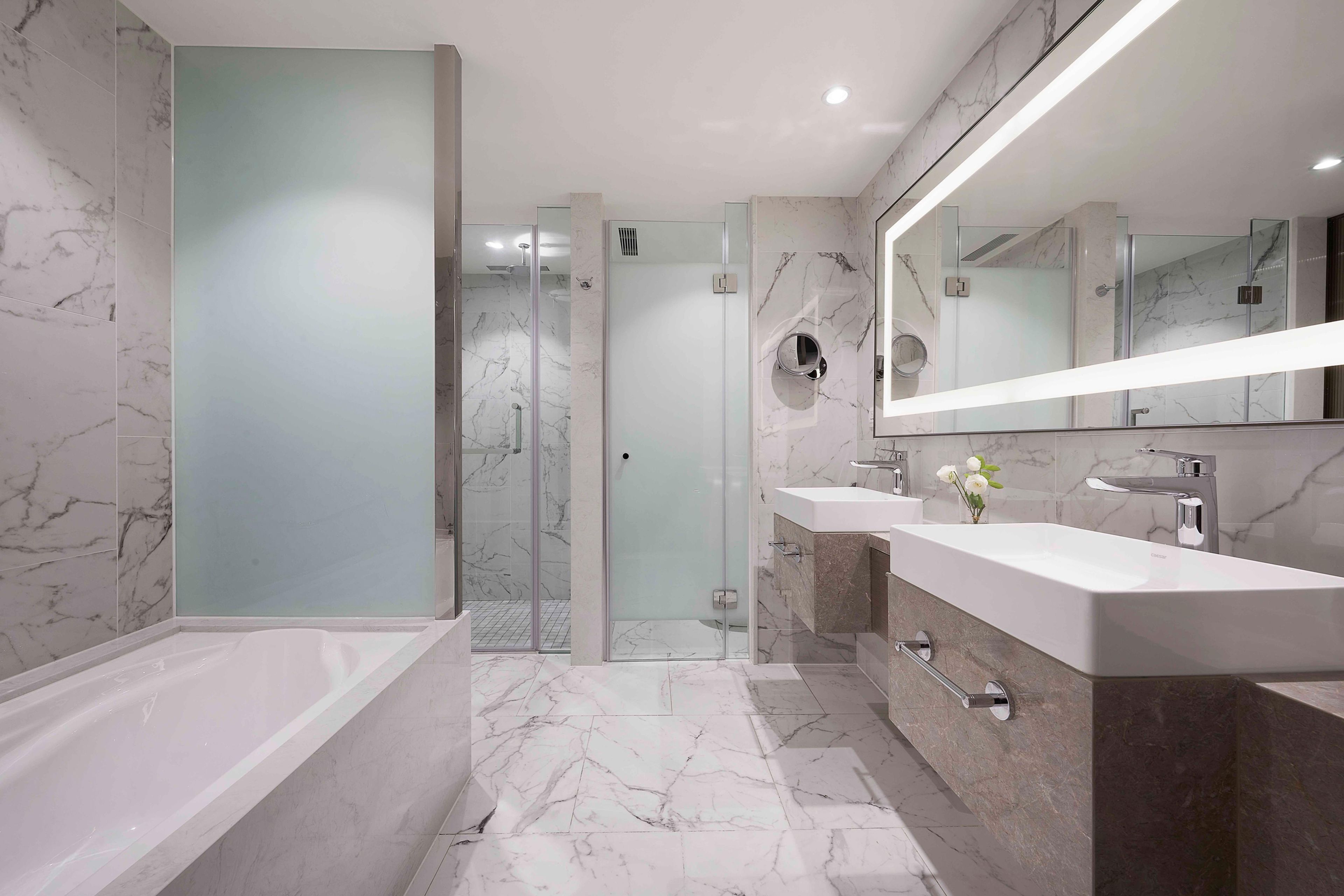 Ein modernes Badezimmer mit einer gläsernen Duschkabine, einem großen Spiegel und einer Badewanne.