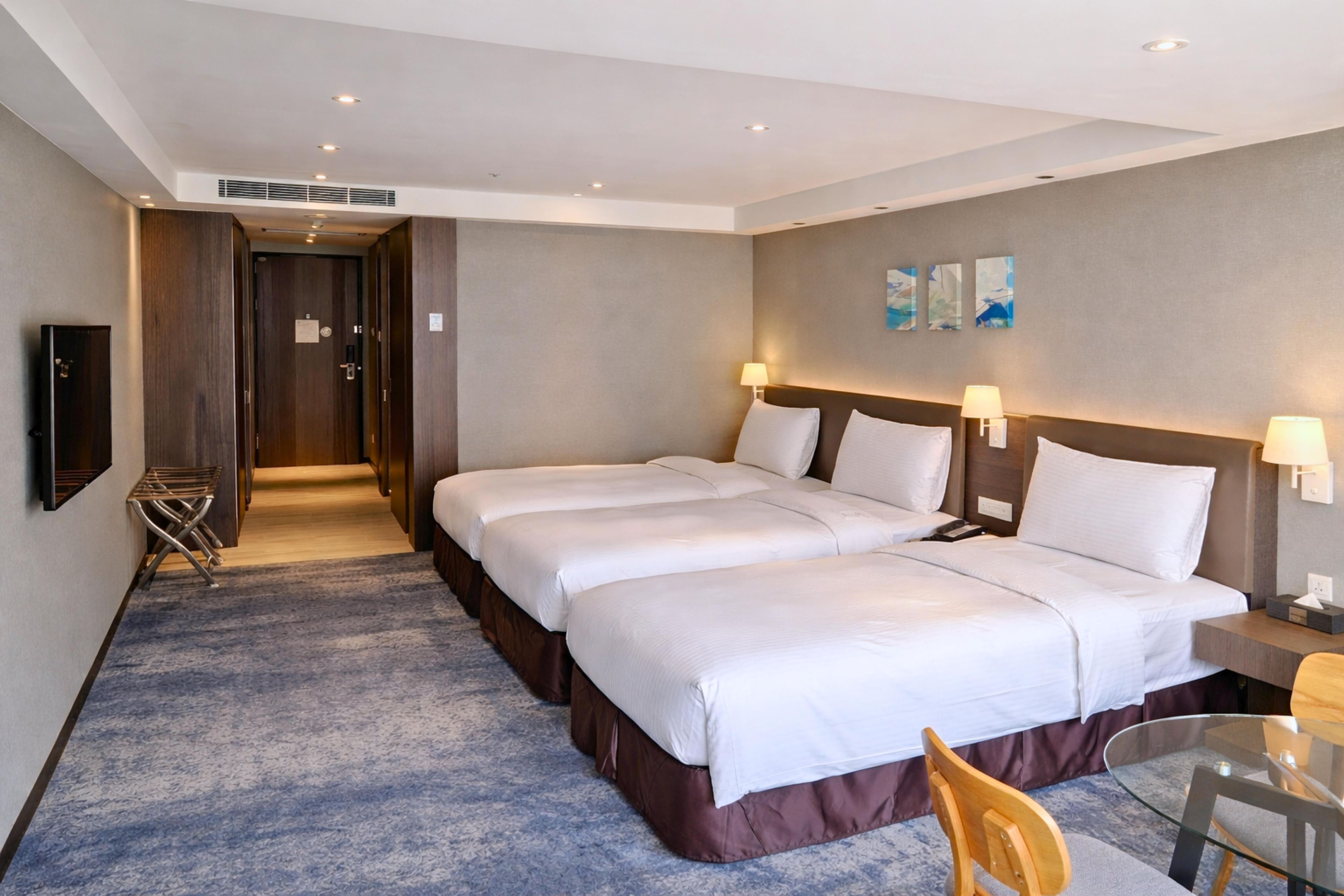 Ein Hotelzimmer mit einem großen Bett, zwei Nachttischen, einem Schreibtisch, einem Sessel, einem Fernseher und einer Tür zum Flur.