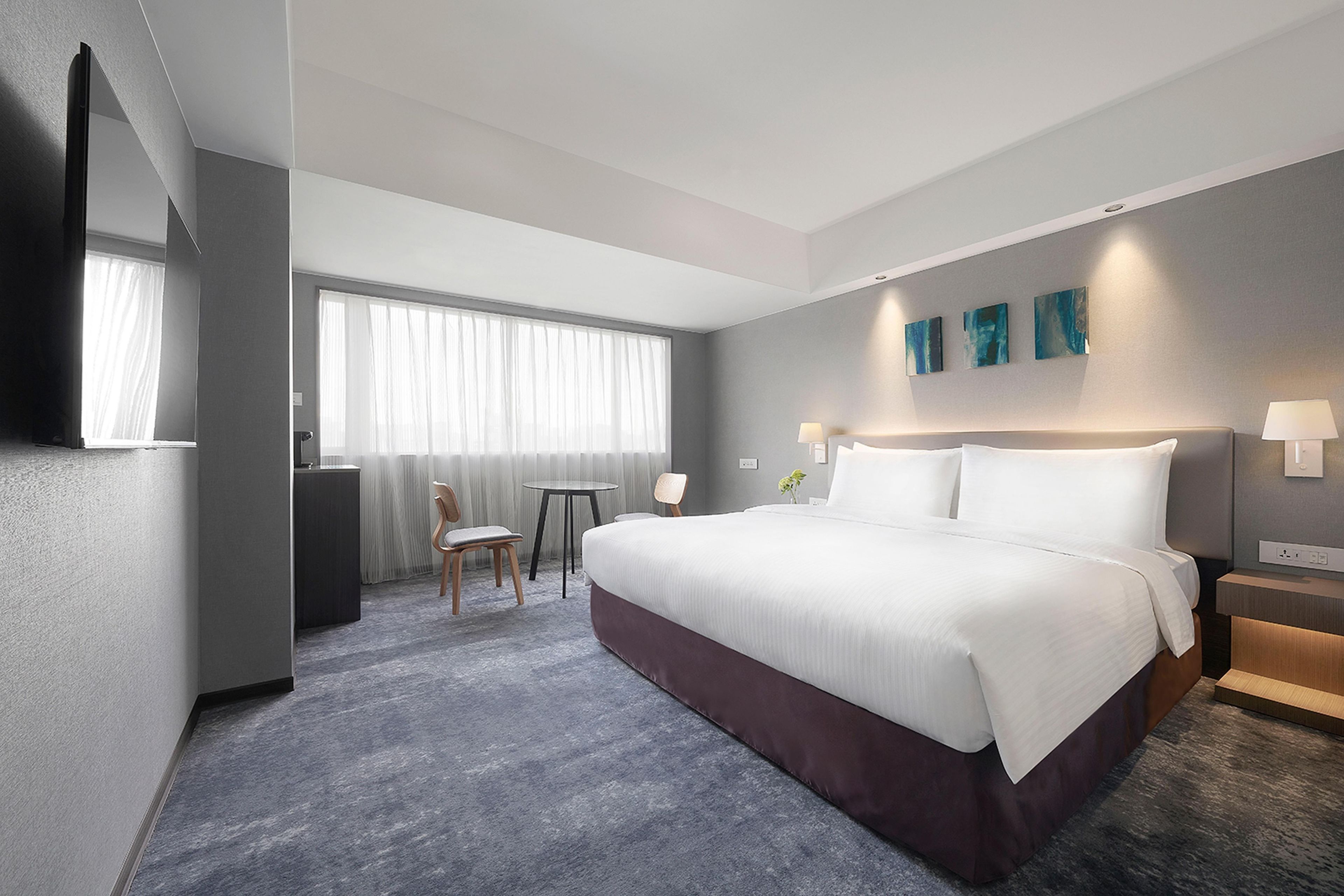 A hotel room with a large bed, a desk, a chair, a small table, and a window with curtains.