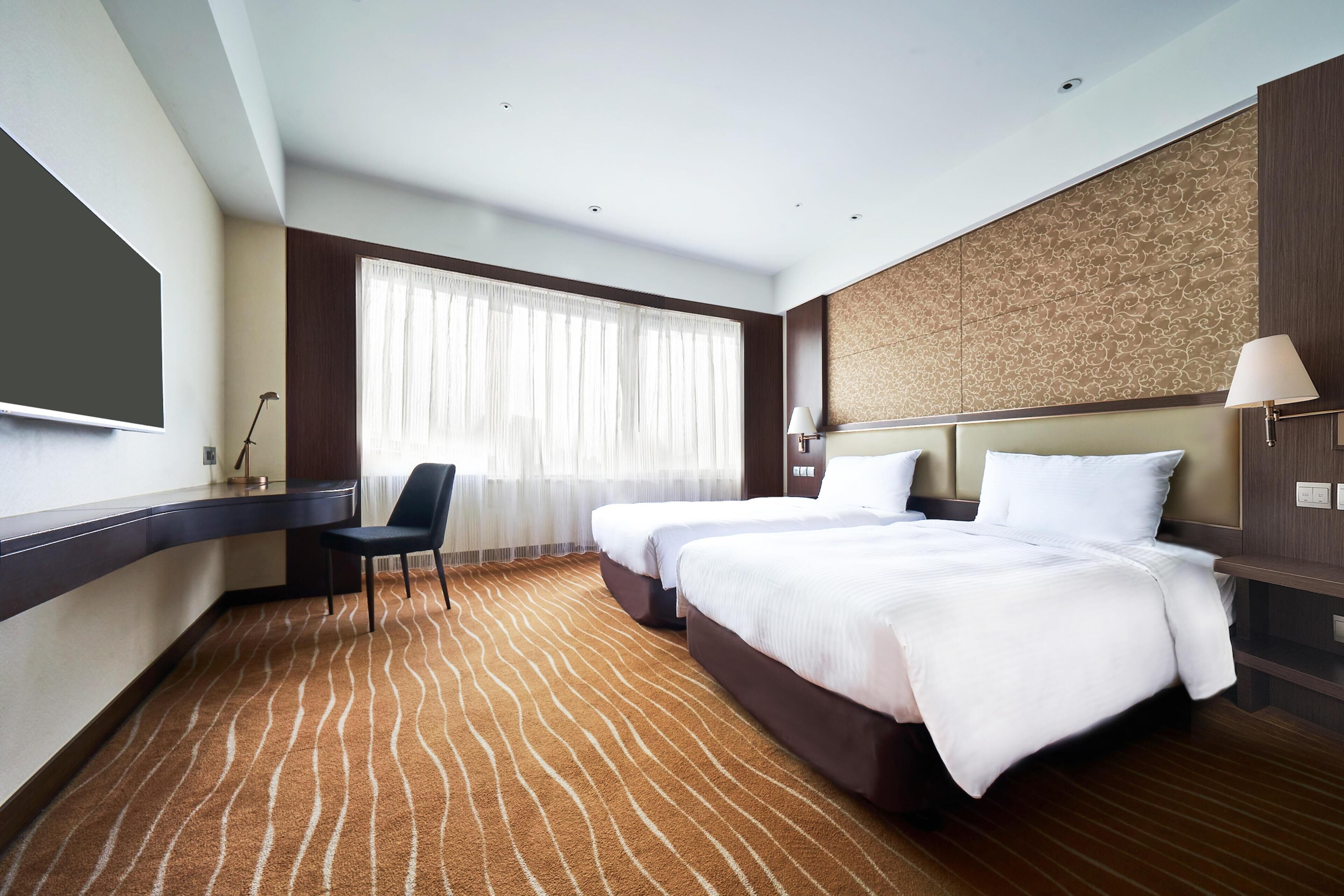 A hotel room with a large bed, a desk, a chair, and a television.