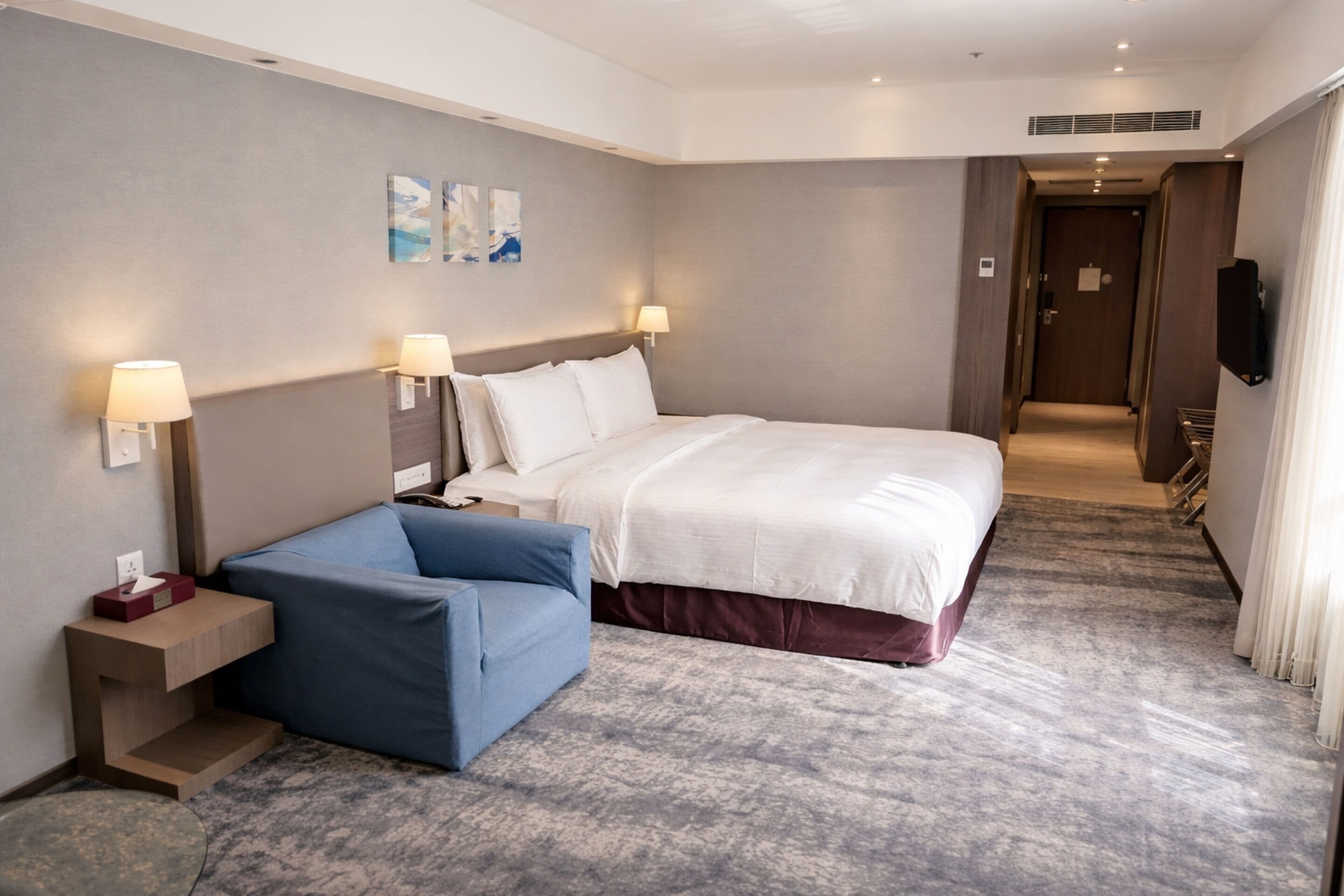 Een hotelkamer met een groot bed, een blauwe bank, een nachtkastje en een aan de muur bevestigde televisie.