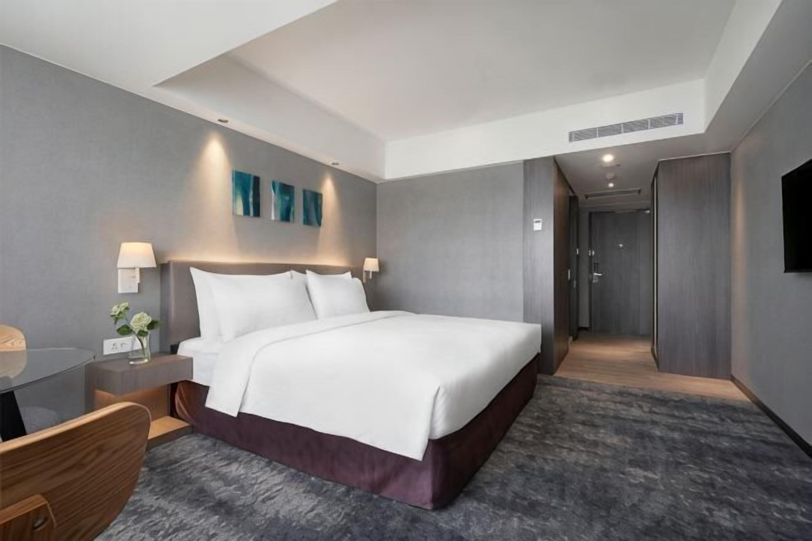 A modern hotel room with a large bed, bedside tables, a desk, and a shower area.