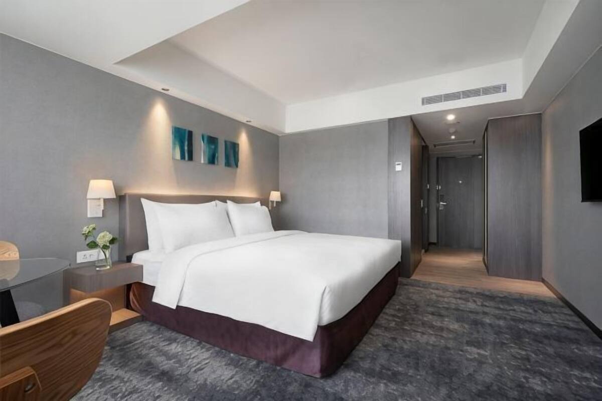 A modern hotel room with a large bed, bedside tables, a desk, and a shower area.