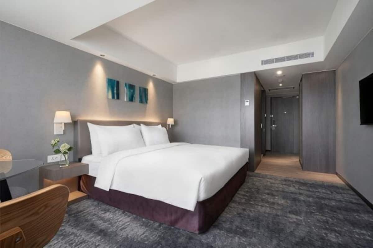 A modern hotel room with a large bed, bedside tables, a desk, and a shower area.