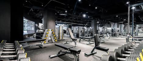 A gym with various exercise equipment, benches, and dumbbells.