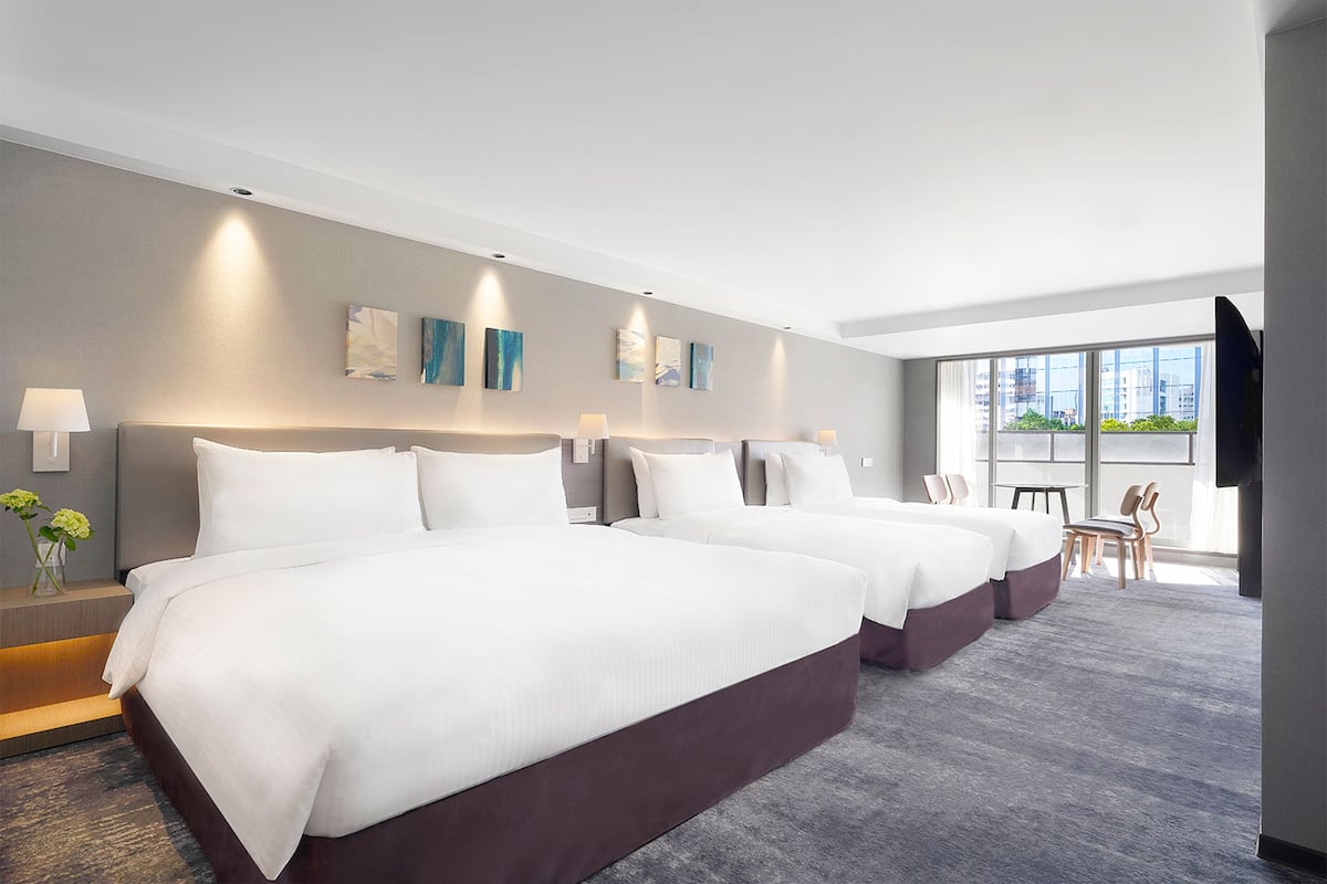 A modern hotel room with three large beds, a small table, and chairs.