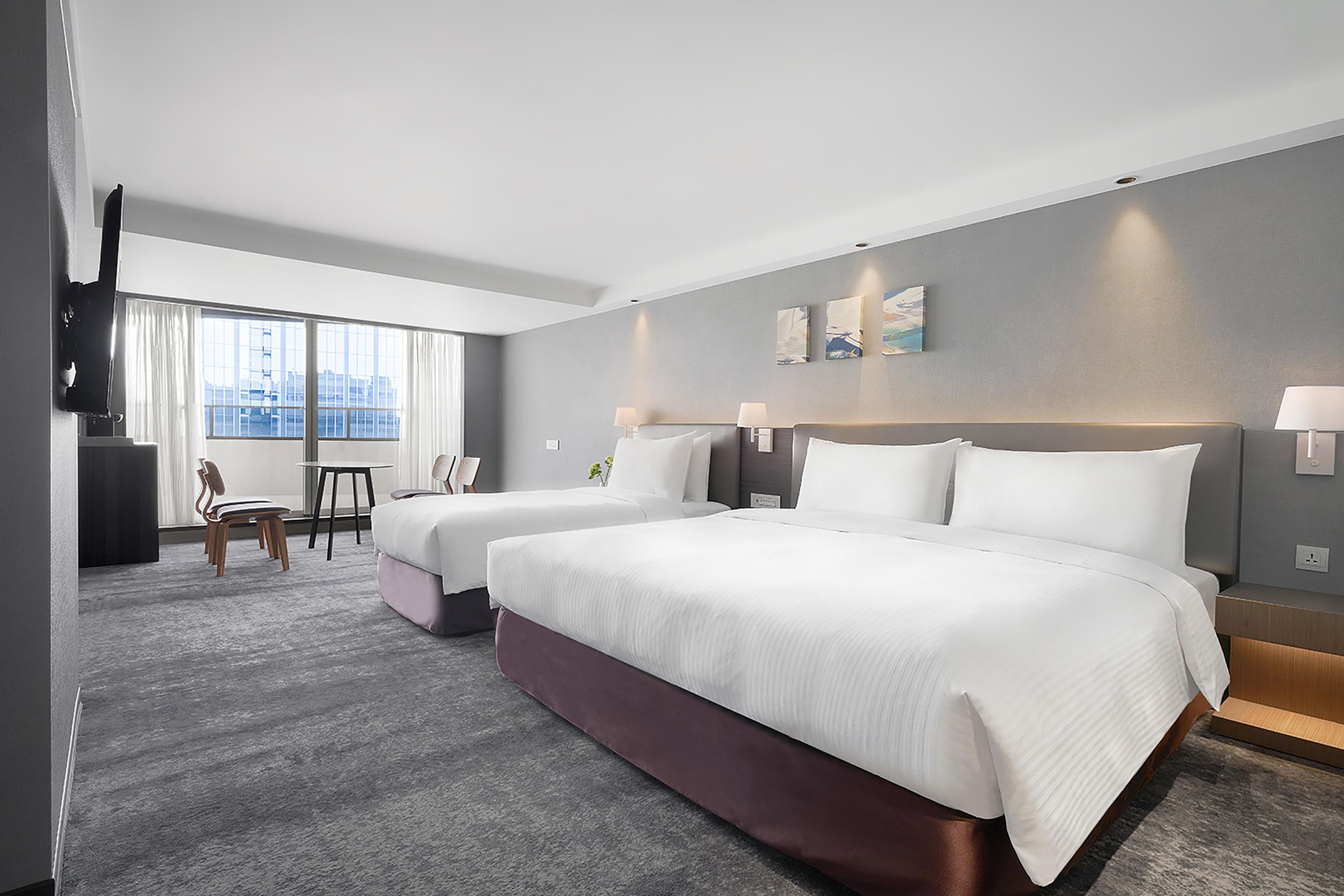 A hotel room with two beds, a desk, and a television.