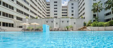 A swimming pool with lounge chairs and umbrellas, surrounded by high-rise buildings.