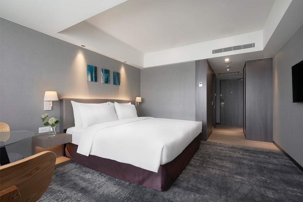 A modern hotel room with a large bed, bedside tables, a desk, and a walk-in closet.