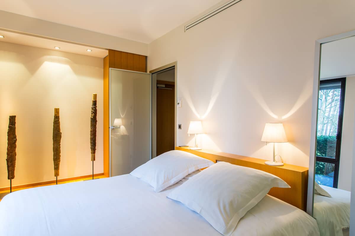 Una camera d'hotel moderna con un letto grande, due lampade ai comodini, un poggiatesta in legno e un ampio specchio.