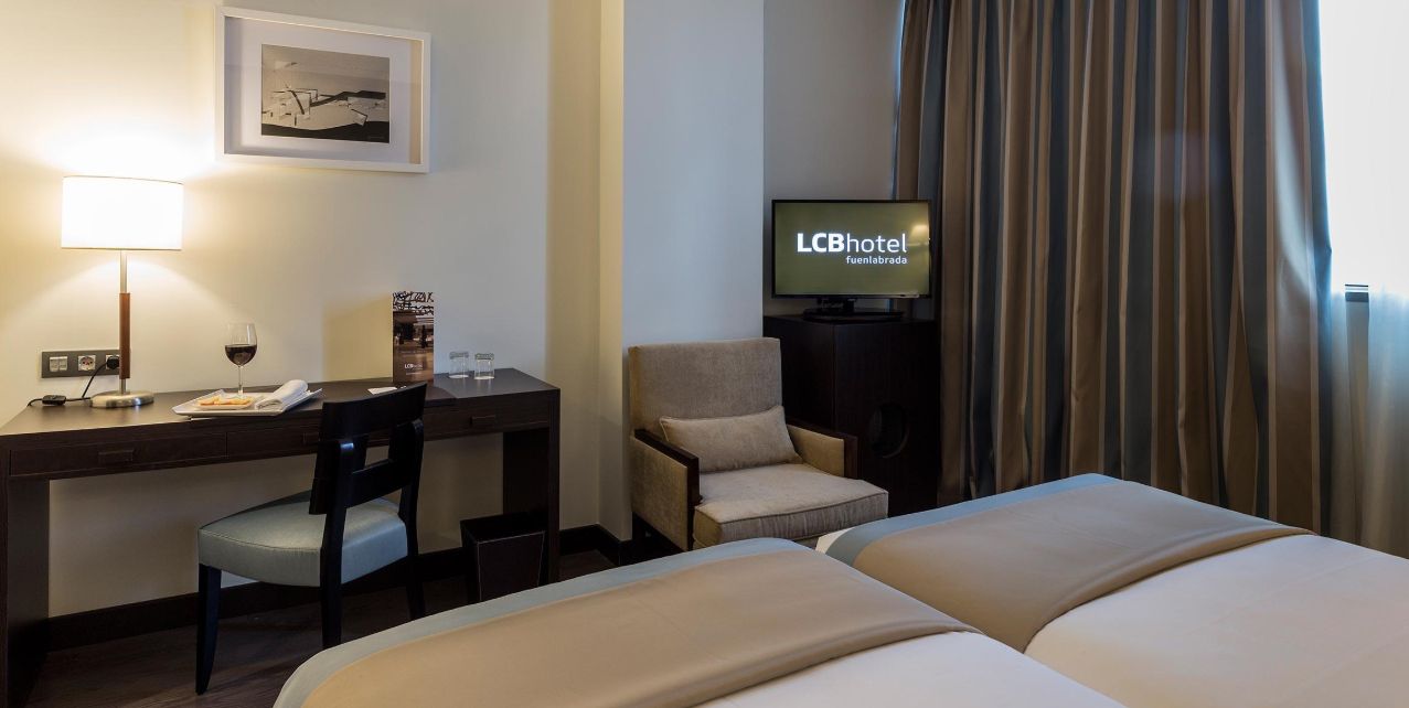 Una habitación de hotel con escritorio, silla, televisión y dos camas.