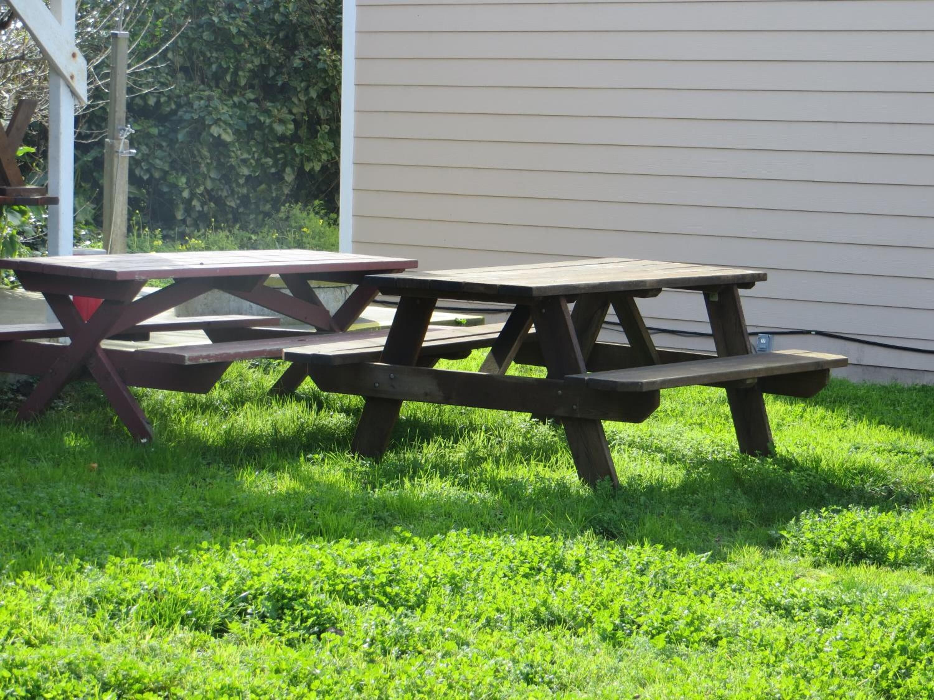 Deux tables de pique-nique se trouvent dans un espace herbeux, avec un bâtiment en arrière-plan.